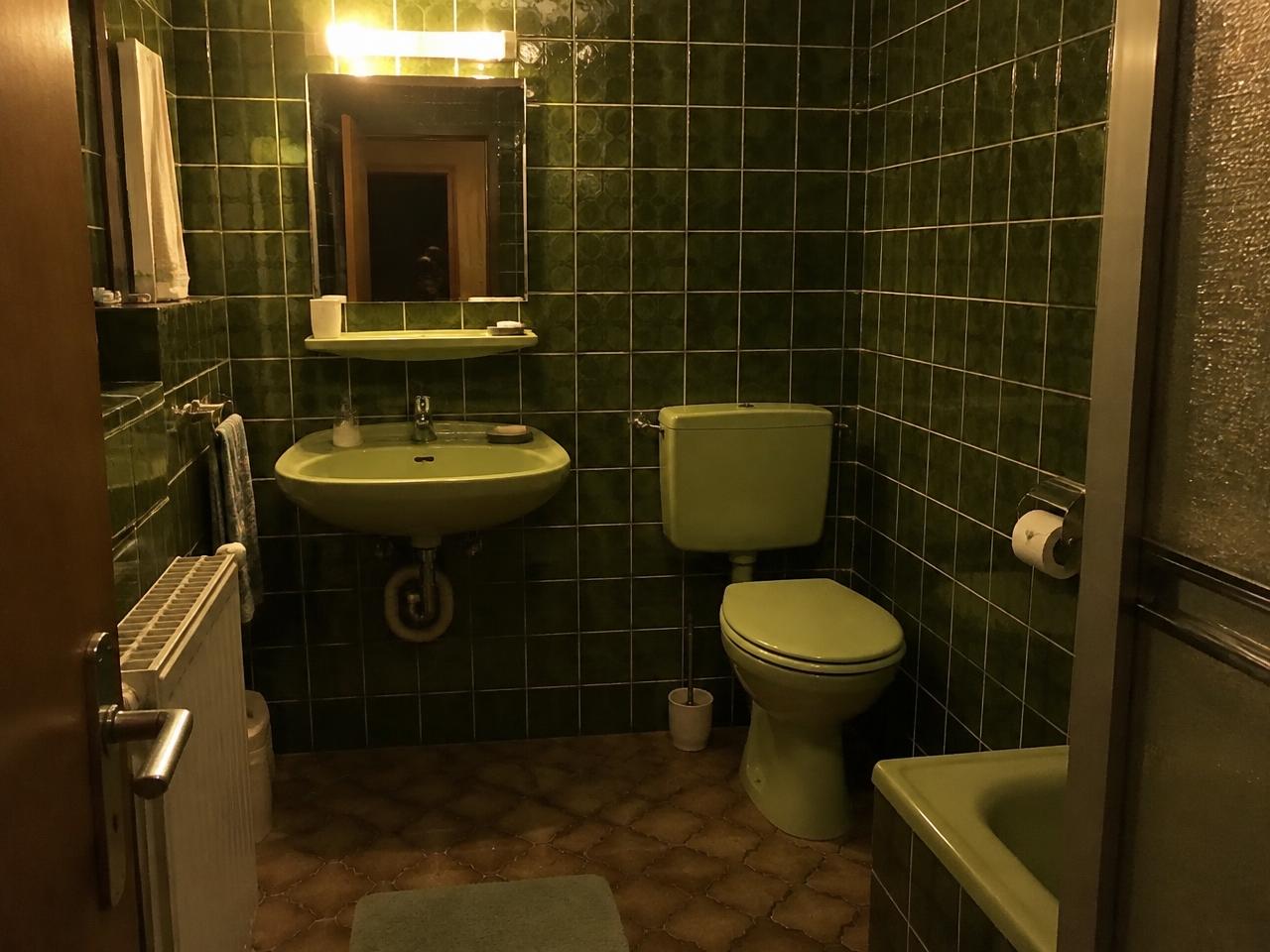 Dunkles Badezimmer aus den 1970er-Jahren mit grünen Fliesen und grüner Sanitärkeramik
