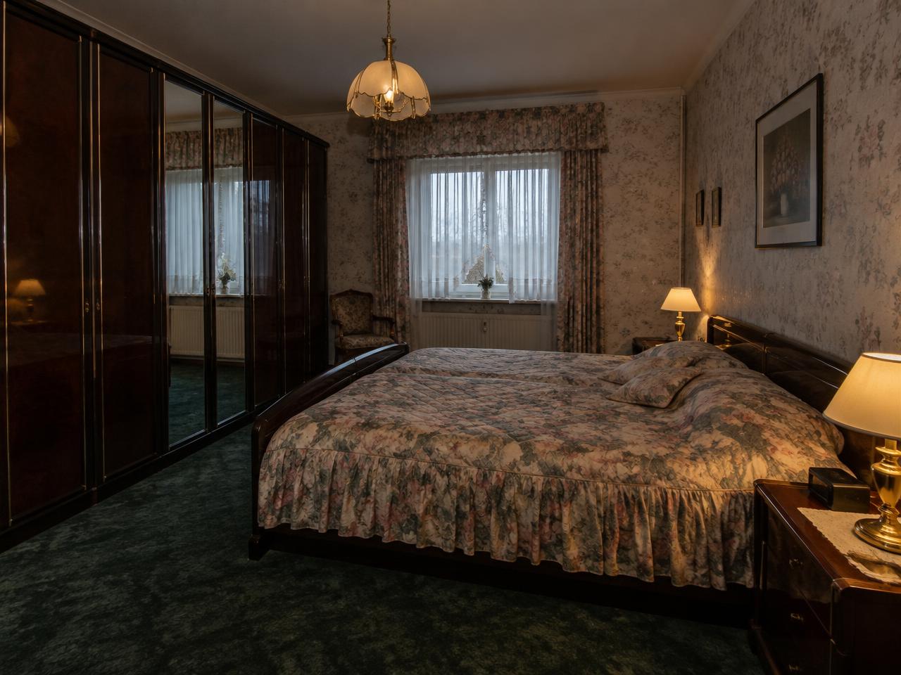 Dunkles Schlafzimmer aus den 1990er-Jahren mit Blümchentapete und grünem Teppich